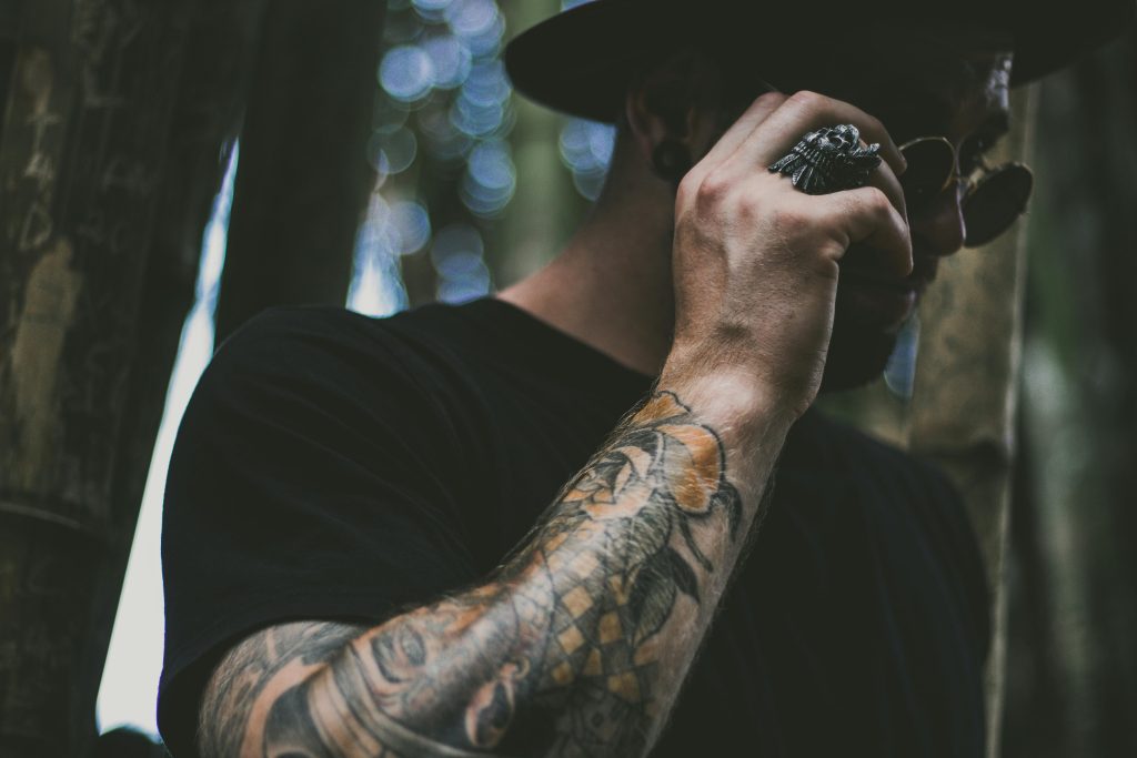 pexels-photo-1662924-1662924 Tattooed man adjusting sunglasses amidst bokeh effect in forest setting.